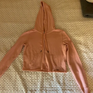 Rosa croppad hoodie från Hollister - Säljer en ljusrosa croppad hoodie från Hollister med dragkedja och huva. Tröjan har långa ärmar, fickor framtill och justerbar dragsko i huvan. Tröjan har knappt använts och är i mycket bra skick.