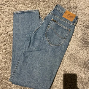 Blå jeansbyxor från Lee - Säljer ett par klassiska blå jeans från Lee i organisk bomull. Byxorna har en rak passform, normal midja och en bakficka med Lee-logga i läder. Perfekta för dig som gillar tidlös denimstil.