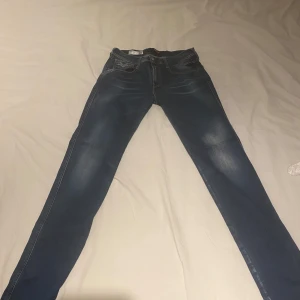 Blå Replay Anbass jeans - Säljer ett par blå Replay Anbass jeans med klassisk femficksdesign och snygga slitningar. Jeansen har skinny passform och raka ben, perfekt för dig som gillar stilrena och bekväma jeans. Märkeslapp bak i midjan och tydliga kontrastsömmar. Buda gärna! FÖRST TILL KVARN!