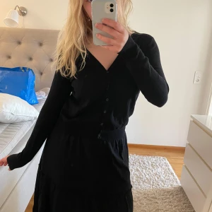 Svart kofta från Zalando Essentials - En klassisk svart kofta med v-ringning och knappar framtill från Zalando Essentials. Långärmad modell i mjukt material, perfekt att slänga över en topp eller klänning. Enkel och stilren design som passar till det mesta.