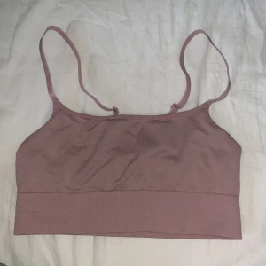 Rosa topp från H&M - Säljer en ljusrosa linnetopp från H&M med tunna axelband och stretchigt material. Perfekt för varma dagar eller som lager under andra plagg. Enkel och stilren design.