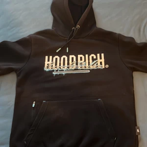 Svart hoodie från Hoodrich med tryck - Säljer en svart hoodie från Hoodrich med stort tryck på bröstet och ryggen. Hoodien har huva med dragsko, magficka och textdetaljer på ena ärmen. Materialet är en blandning av bomull och polyester. Denna tröjan är för liten för mig. Den är knappt använd och i mycket bra skick.