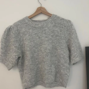 Ljusgrå stickad tröja från Vero Moda - Supermjuk ljusgrå stickad tröja från Vero Moda med korta ärmar och rund hals. Tröjan har en lätt puff vid axlarna och ribbade kanter vid ärmslut och nederkant.