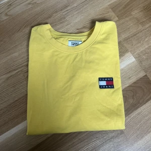 T-shirt ifrån Tommy Jeans - Snygg gul t-shirt ifrån Tommy Jeans. Passformen på t-shirten är croppad och rakare.  Storlek XL men passar mig som har L. Kan skicka fler bilder vid intresse.  Knappt använd. 