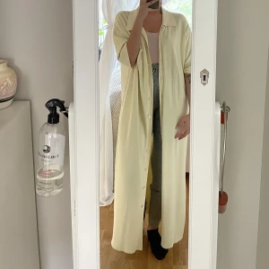 Lång skjortklänning/cardigan från HOPE - Denna pastelgula klänningen/cardigan går att använda på många sätt. Funkar att ha den knäppt hela vägen eller öppen över andra plagg. Slits nere vid sidorna. Världens skönaste material!   Ordinarie pris: 3400kr
