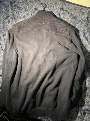 Hugo kofta - Säljer en Hugo kofta som passar både storlek M-L och är i ett bra skick trots användningen. Saknar den delen man drar i men trots det fungerar dragkedjan bra. 