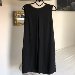 Klänning svart - Tunn svart klänning för fest eller vardag, gulddetaljer.  Storlek 42. Tunn guldkant kring hals. Guldspänne i nacken. Liten öppning upptill i ryggen. Ej genomskinlig.