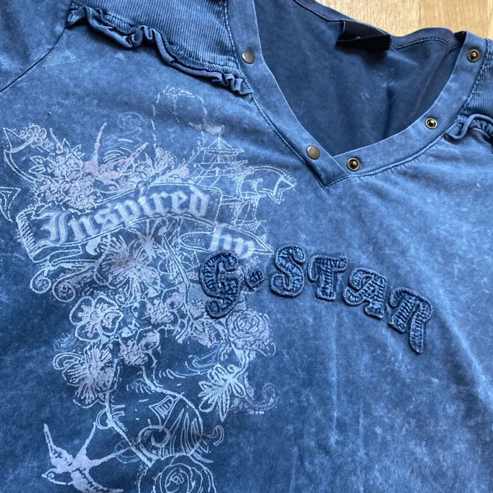 En extremt snygg ljusblå tröja med ännu snyggare detaljer! Ett tryck på framsidan likt Affliction och volangliknande axlar, samt fungerande knappar längs tröjans krage! Väldigt skönt material, perfekt för sommaren! Står storlek 4, sitter som en M. T-shirts.