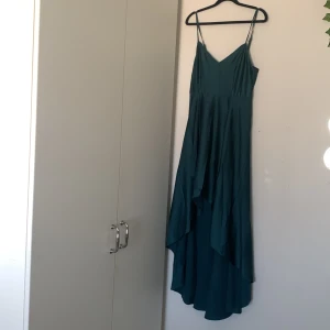 Klänning  - En fin klänning som är som en balklänning. Är som sillkes material i mörk grön med dragkedja på bak sidan. Är kortare där fram då de går upp i volang.