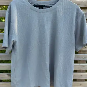 En ljusgrå t-shirt i rak modell som glittrar i silver. Lindex, stl M. Använd vid ett tillfälle.