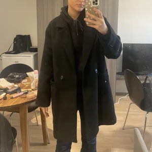 Svart kappa - Svart knälång kappa från Pull and bear. Sparsamt använd så den är inte nött eller har märken på användning. Säljer då den inte kommer till användning