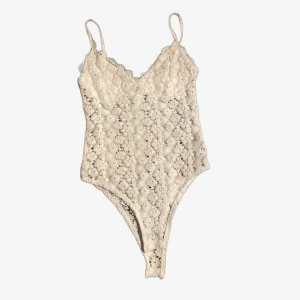 Body - Broderad body med vitt blommönster. Oanvänd, bra kvalitet! Fäster bodyn där nere med två knappar.