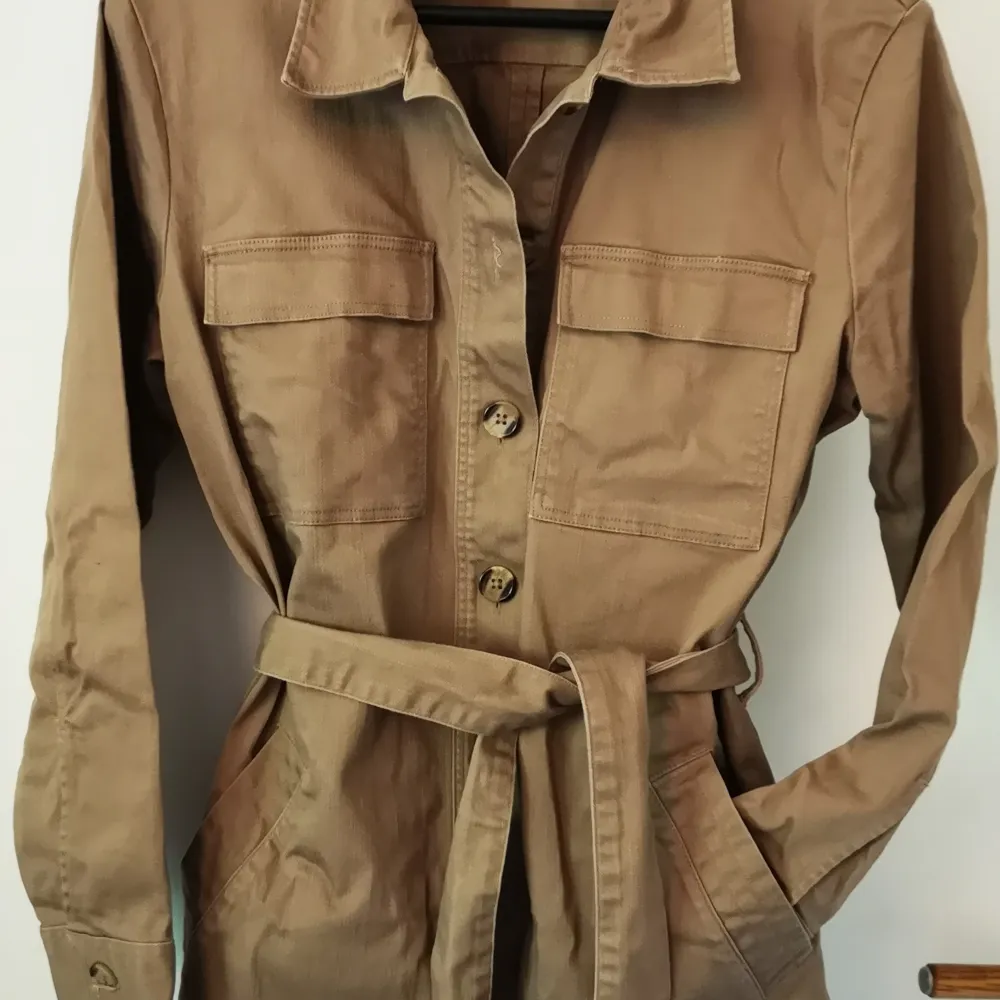 Brown denim overshirt or light jacket (depends how you dress it). Buttons, breast pockets and waist pockets and a waist belt. . Jackor.