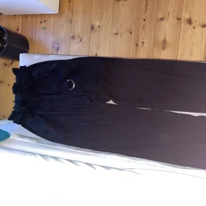 Långa kostymbyxor i storlek XS - Långa svarta kostymbyxor i storlek XS. Har ett tillhörande bälte som man knyter runt. Supersnygga och lätta i materialet. Skulle säga att de passar från 165 till 175 beroende på hur man vill att de ska sitta i län