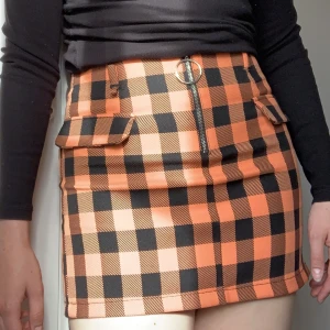 Rutig Minikjol - Stretchigt material, dragkedja fram och öglor för bälte. Fickorna fram är fake.