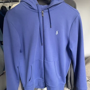 Ralph lauren zip hoodie  - Lila/blå raplåt lauren zip hoodie. Skick 8/10. Den är använd men har ett väldigt fint skick. Nypris 1700kr, storlek S passar M