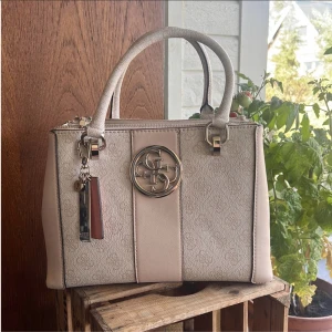 Guess väska  - Säljer min guess väska i modellen BLUEBELLE STATUS STATCHEL i nyskick, använd 3 gånger under 2 år, därav priset. Har tyvärr inte kommit till användning, nypris 1500kr. Tillhörande dustbag medföljer och axelrem om man vill ha de🌸 