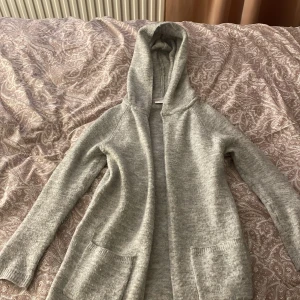 Grå mjuk kofta - En fin grå mjuk kofta som har två fickor och en luva. Den har inte en dragkedja så den går inte att knäppa igen men den är mjuk och skön. Den är inte heller så lång. Den är storlek 140 men den passar som XS.Skriv för mer bilder och tryck gärna på köp nu! 