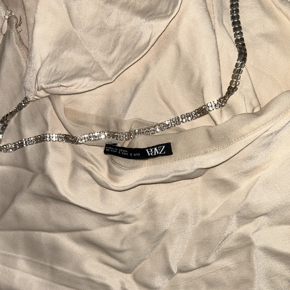 Fallklänning från Zara i glansigt/silkesaktigt tyg. Kedja i strass runt halsen och öppen rygg. PytteSmå fläckar bak på klänningen (syns på bild) försvinner vid tvätt.   . Klänningar.