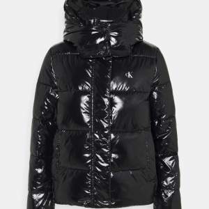 En glansig svart jacka i fint skick från Calvin Klein. Den har även en avtagbar luva. ordinarie pris 2200