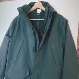 Fodrad långjacka - - Lätt fodrad med huva - Aldrig andvänts helt ny - mörkgrön - 4 fickor. Inga innefickor