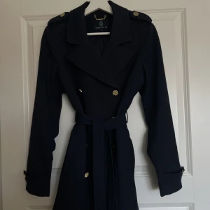 Jacka - Blå trenchcoat med guldknappar från Stockhlm. Storlek 38.