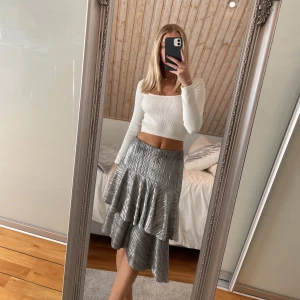 Silvrig kjol - Silvrig/glittrig midikjol från Nelly med volanger! Superskön och sval. Fint skick. Köparen står för frakt.