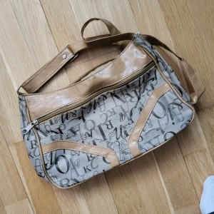 Y2K axelväska med mönster - Inköpt mellan år 2000-2010. Frän Y2K axelväska med mönster. Väldigt fin men har lite skavanker, se största exemplet på bild. Minns ej skicket inuti. Kan ta fler bilder och kolla detta. Svarar på alla frågor. 