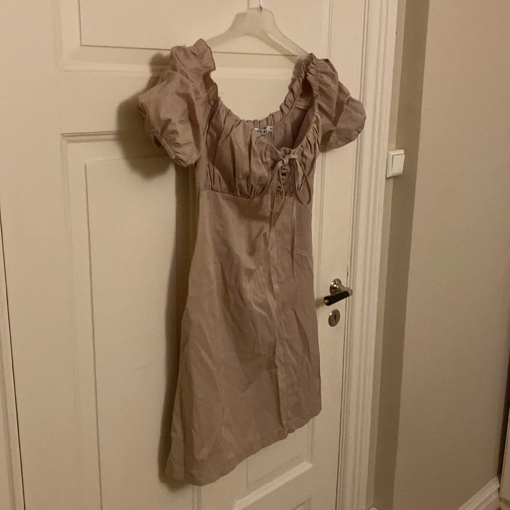 Säljer denna snygga klänningen från NA-KD. Oanvänd. Storlek 40, men lite liten i storleken. Snygga detaljer vid axlarna och framtill. Off-shoulder. Färgen är beige. . Klänningar.