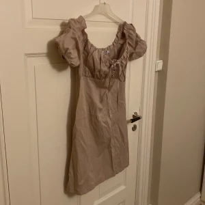 Klänning från NA-KD  - Säljer denna snygga klänningen från NA-KD. Oanvänd. Storlek 40, men lite liten i storleken. Snygga detaljer vid axlarna och framtill. Off-shoulder. Färgen är beige. 