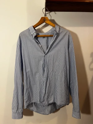 Skjorta COS  - Klassisk vit och blå randig skjorta från COS, sitter snyggt oversize på mig som brukar ha S.