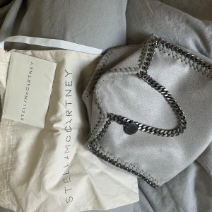 Stella McCartney väska - Jätte söt Stella väska i modellen tiny! Köptes på plick för nått år sen så kan ej säkerställa att den är äkta, därav priset. Har dustbag samt lappar kvar. Modellen heter falabella med! Finns en liten defekt på knappen som ni kan se bild 2