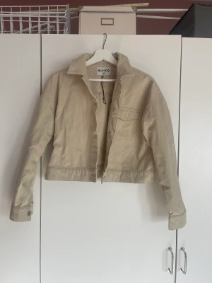 Vårjacka - 💛Vårstädning av garderob 💛  Vårjacka från NA-KD. Croppad jeansjacke i beige, med en ficka på bröstet. Fint skick. 
