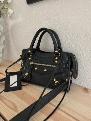 Balenciaga Mini City Bag - Säljer min Balenciaga mini city bag i svart med gulddetaljer. Köptes på NK i Göteborg för 10 490kr. Dustbag och kvitto finns.   Väskan är sparsamt använd men förekommer små slitningar på, se bilder. Inget som syns när man använder den.