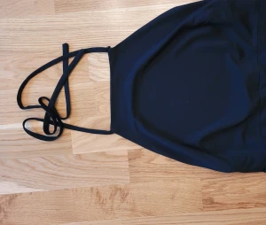 Svart halterneck jumpsuit  - Svart halterneck byxdress med öppen rygg. Band knyts i nacken antingen träs banden genom flärpen på ryggen eller så viker man ner flärpen så ryggen blir helt öppen. Sitter tight över rumpan och blir sen vidare i benen. Står inte storlek, sitter som S