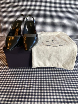 Prada svarta klackskor - Svarta läder slingback klackskor ifrån Prada (7 cm klack). Skorna är i gott skick. Orginal skopåse och kartong medföljer.