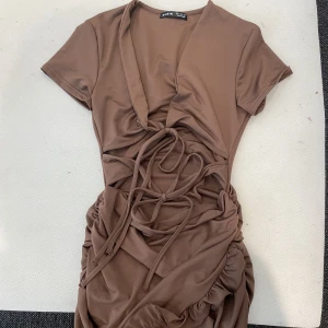 Brun klänning  - Brun klänning som är lite öppem framtill, visar lite hud men absolut inte för mycket.  Går till ovanför knäna