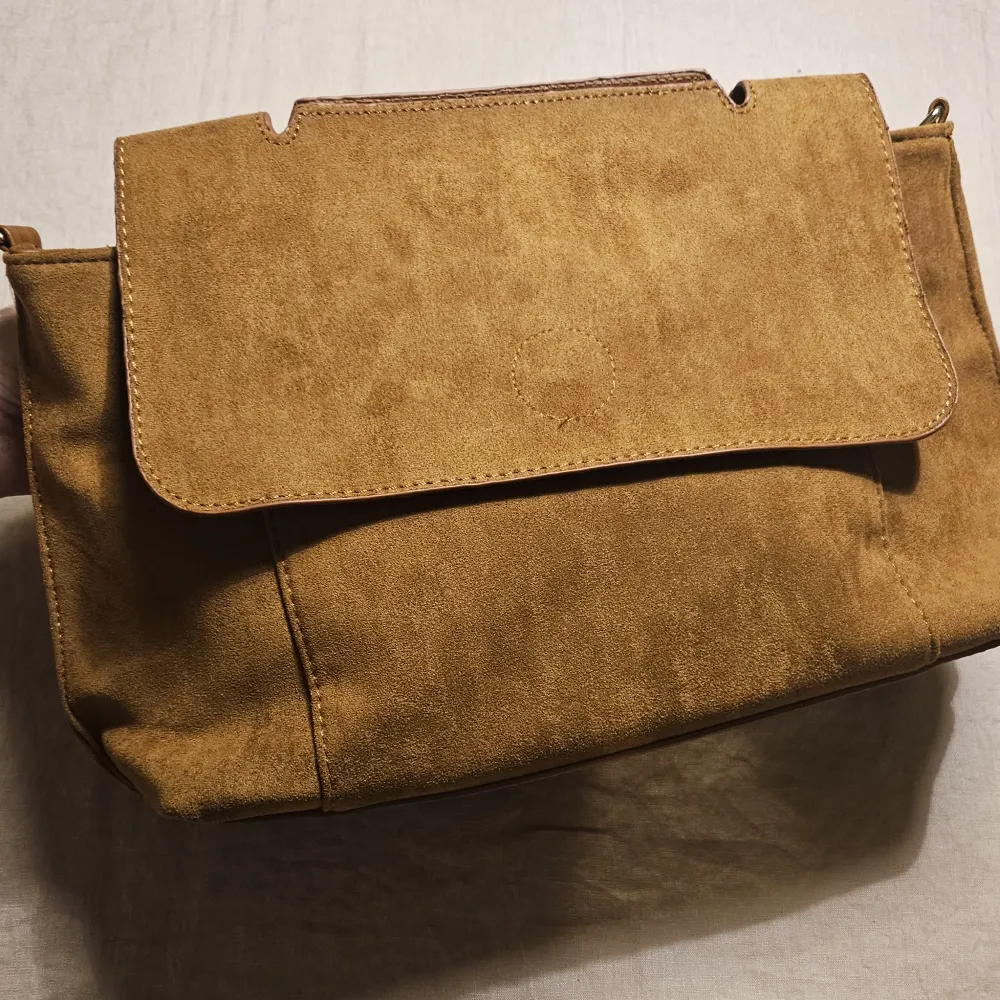 Helt oanvänd medelstor kamelfärgad handväska i veganskt läder och mockaimitation.  Avtagbar och reglerbar väskrem.. Väskor.