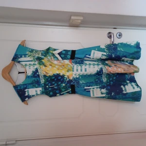 Scubaklänning med tryck i smickrande modell - Dramatisk klänning i scuba med tryck och utställd kjol samt bälte i midjan. Tyget är rejält stretchigt och stadigt vilket är smickrande för figuren. 