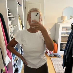 Volang blus - En vit t-shirt med volanger vid ärmarna från Bik Bok. Blusen är i storlek s och är använd med i ett fint skick.