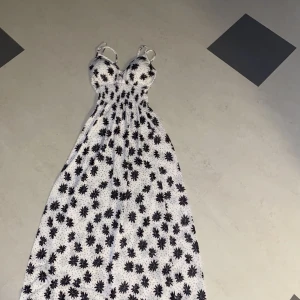 Blommig långklänning  - Aldrig använd! Asbra skick, köpt någon gång i somras. Den har vaddering vid bysten.  Vit med svarta blommor. Den är väldigt strechig, alltså den passar S och L också. Jag är 162 och den når ner till mina fötter när man har den på sig.