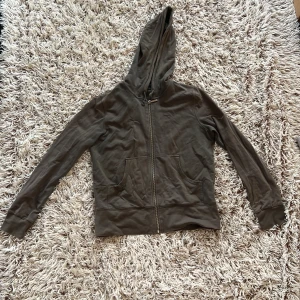Brun hoodie med dragkedja från Lindex - Mjuk brun hoodie från Lindex i storlek M. Tröjan har dragkedja framtill, huva med snörning och två fickor. Tillverkad i bomull. Perfekt för chill dagar eller när du vill ha en enkel och stilren look. En 2000-tal kofta från Lindex.  Koftan är stretchig.