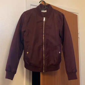 Vinröd bomberjacka  - En vinröd bomberjacka. Ett litet litet sträck sträck på höger arm men inget man tänker på