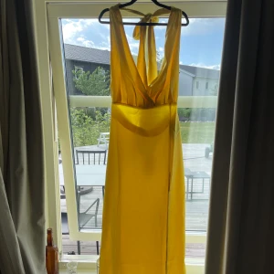 Maxiklänning i satin - En superfin gul maxiklänning med öppen rygg och slits framtill. Den är helt ny och oanvänd från NAKD med prislappen kvar. Verkligen så drömmig och fin men är tyvärr för liten. Är från Josefine HJs kollektion tillsammans med NAKD. Passar en både en S och M