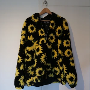 Fin TeddyJacka med solrosmotiv - Fin jacka i teddytyg med solrosmotiv, vindtät och med en svart luva. Jackan är från BoohooMan i storlek M