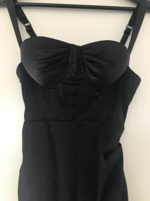 Svart satinklänning - Svart satinklänning, slits på vänster sida och rynkade sidor. Superfin, aldrig använd, endast provad, lapp kvar. XS/34 dock lite liten i storleken 