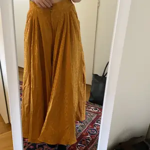 Jättehärlig gul/orange lång ”kjol”- som faktiskt är en byxa med fickor som man ser på sista bilden. Superfint tyg (100% buret svila) stl 14/158. Jättefint skick. OBS kan skickas fram till onsdag 30/8. 