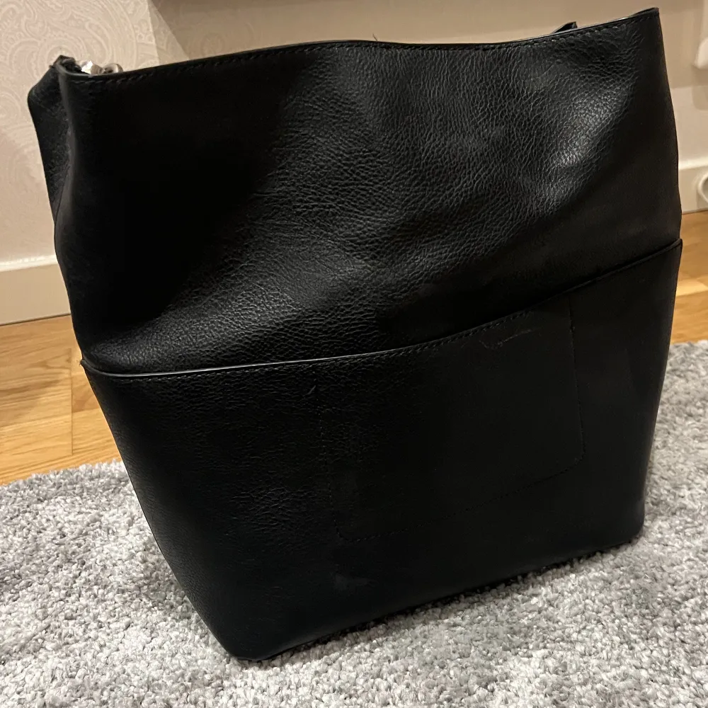 En svart väska i läder från Åhléns, mycket rymlig med en avtagbar organiseringsficka. Väskan är i nyskick och perfekt för skolan❤️. Väskor.