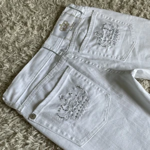 Utsvängda Victoria Beckham jeans - Vita Victoria Beckham jeans. ❤️ Lågmidjad och bootcut modell med silverkronor och rhinestones på bakfickan. Storlek står ej. Är 165cm, innerbenslängden är 80,5 och midjemåttet 36 rakt över. Håll koll på min profil, säljer för det mesta vintage jeans! 😍