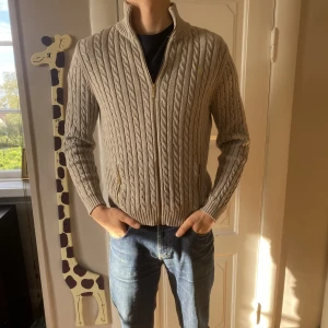 Ralph Lauren Kabelstickad fullzip  - Väldigt stilig Kabelstickad fullzip som är perfekt till vintern. Modellen i bilden är 177Cm. Tröjan har inga defekter och därför säljer jag den för 549kr kontra original priset som ligger på 1699. Den är L i dam men passar S i herrar.